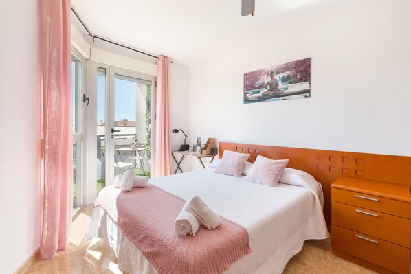 A bedroom with a bed, a nightstand, a window with curtains, and a painting on the wall.
