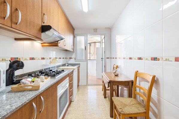 Una cocina con armarios de madera, una estufa a gas, una cafetera y un comedor con mesa y sillas de madera.