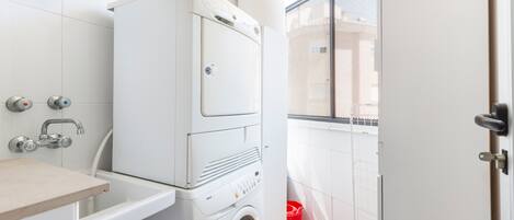 Un lavadero con lavadoras y secadoras apiladas, un lavabo y un cubo de basura rojo.