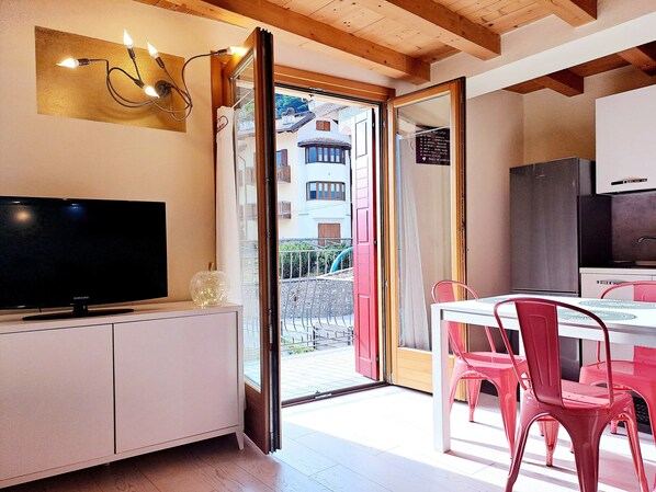 A modern kitchen with a dining area, a television, and a sliding glass door leading to an outdoor balcony.