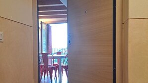 Un pasillo con una puerta de madera, un felpudo y vista a un comedor con sillas y mesas.