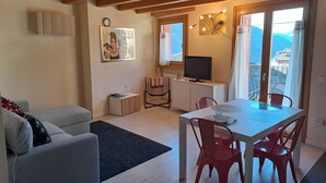 Una sala de estar moderna con un sofá, una mesa de comedor con sillas, un televisor y vistas a montañas a través de amplios ventanales.