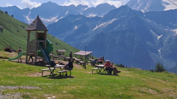 Un parque infantil con toboganes y mesas, con montañas al fondo.