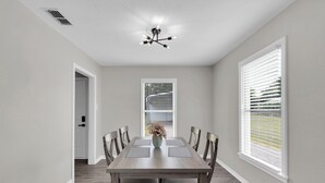 A dining room with a wooden table, chairs, a vase with flowers, and a ceiling light fixture. - A Gem on 5th St (Tyler)