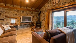 A stone-walled living room with a fireplace, a television, and a sofa. - Country House 'El Paraiso Del Yayo' with Mountain View, Private Terrace and Wi-Fi (Cantabria)