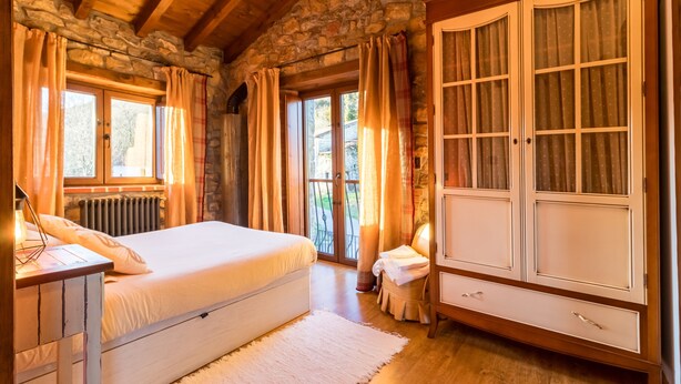A bedroom with a bed, a dresser, a window with curtains, and a stone wall. - Country House 'El Paraiso Del Yayo' with Mountain View, Private Terrace and Wi-Fi (Cantabria)