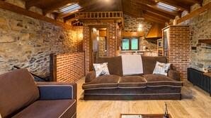 A cozy room with a stone wall, wooden ceiling beams, a brown sofa, and a brick fireplace. - Country House 'El Paraiso Del Yayo' with Mountain View, Private Terrace and Wi-Fi (Cantabria)