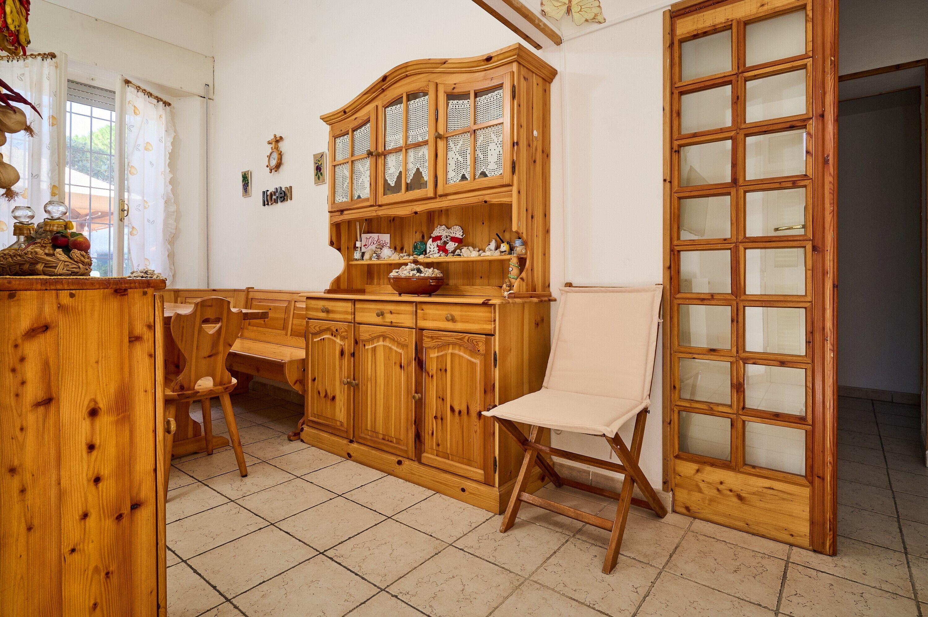 A wooden cabinet with glass doors, a white chair, and a tiled floor.