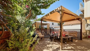 Un espace extérieur abrité, avec une table et des chaises, entouré de plantes et d’une clôture.