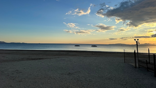 Une plage avec un ciel dégagé, une mer calme et une terre visible au loin.