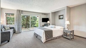 A bedroom with a bed, a TV, a desk, a chair, and a window with curtains.