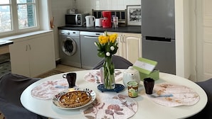 A kitchen with a dining table, chairs, a refrigerator, a washing machine, and a window.