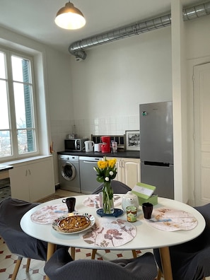 Une cuisine équipée d’une table à manger, de chaises, d’un réfrigérateur, d’un lave-linge et d’une fenêtre.