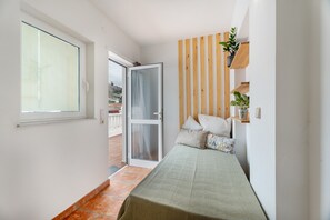 A narrow room with a bed, a sliding glass door, and a wooden slat wall.