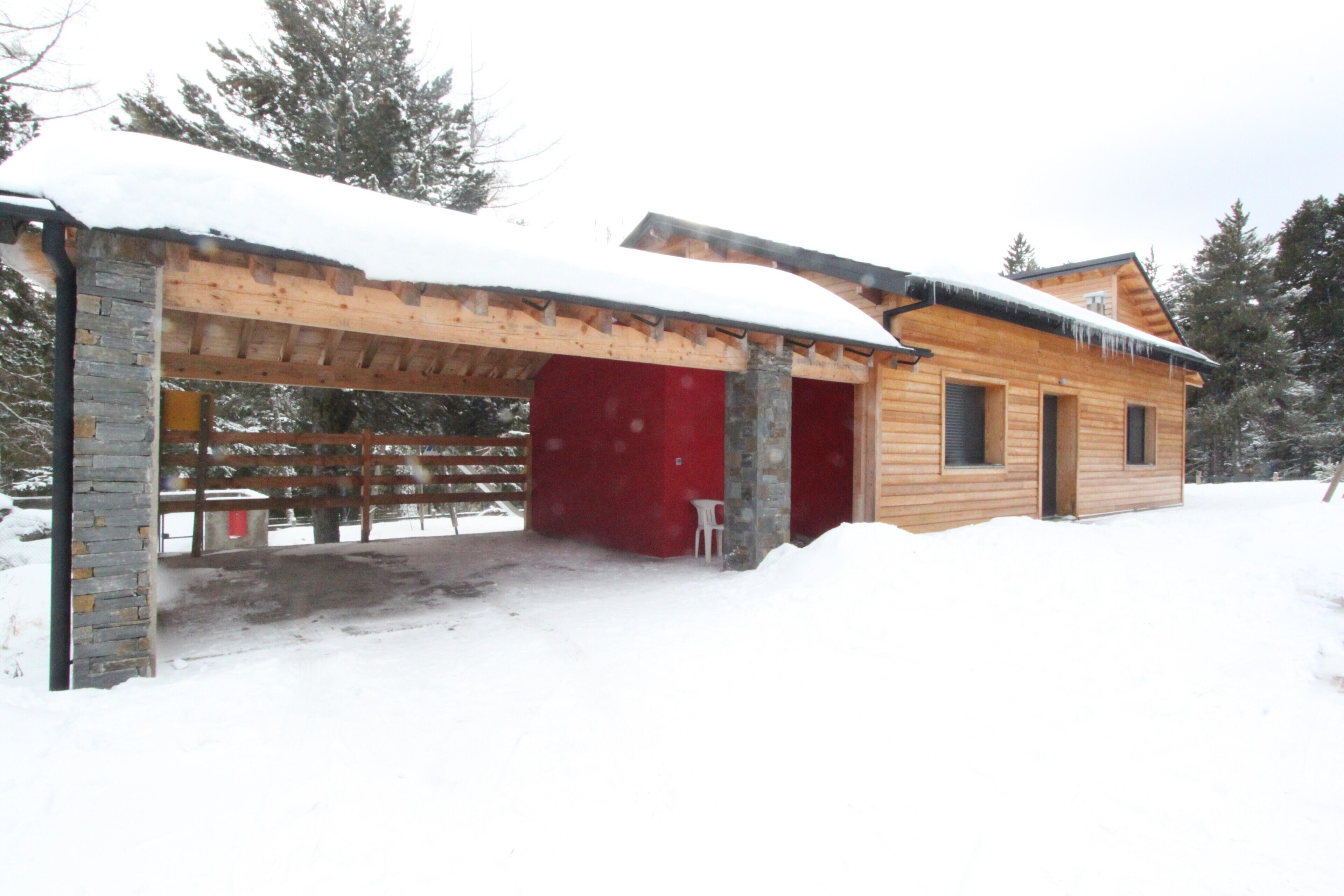 Una cabaña de madera con puerta roja, un porche cubierto y un techo cubierto de nieve.
