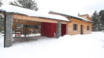 Una cabaña de madera con puerta roja, un porche cubierto y un techo cubierto de nieve.
