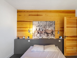 Ein Schlafzimmer mit einem hölzernen Kopfende, einem Bett mit weißer Bettwäsche, einem an der Wand hängenden Bild von Hirschen und einer Tür mit Holzeinlage.