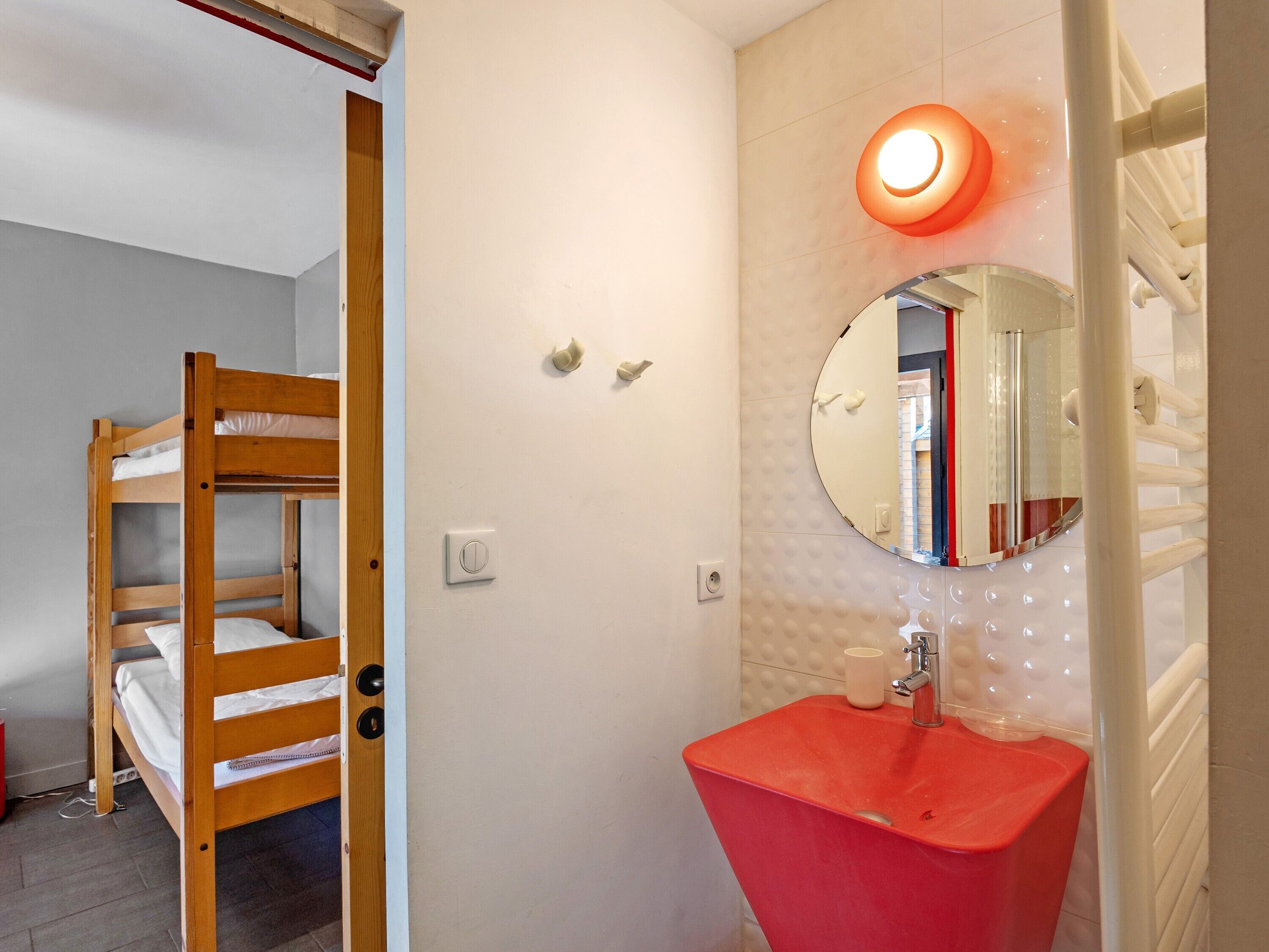 A bunk bed, a red sink, a mirror, and a light fixture in a room.
