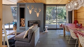 A modern interior with a wooden ceiling, a fireplace, a sofa, a dining table with chairs, and a large window offering a view of the outdoors. - Modern Family Chalet with Mountain View, Private Terrace and Wi-Fi (Bolquère)