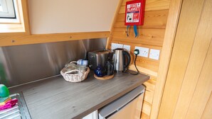 Una kitchenette con tostadora, hervidor y cafetera de acero inoxidable sobre una encimera de madera. Hay una manta ignífuga montada en la pared sobre la encimera.