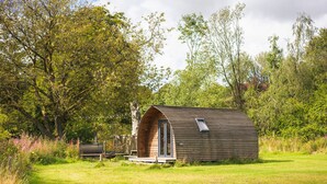 A small, wooden cabin with a curved roof, surrounded by lush greenery and trees.