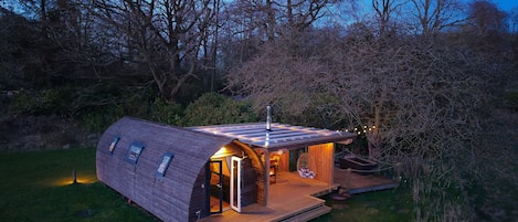 A modern, semi-open structure with a sloped roof, a wooden deck, and a small porch area.