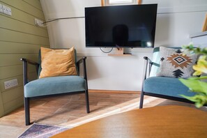 Ein Zimmer mit zwei Stühlen, einem Tisch, einem flachbildfernseher an der Wand und einem Fenster.
