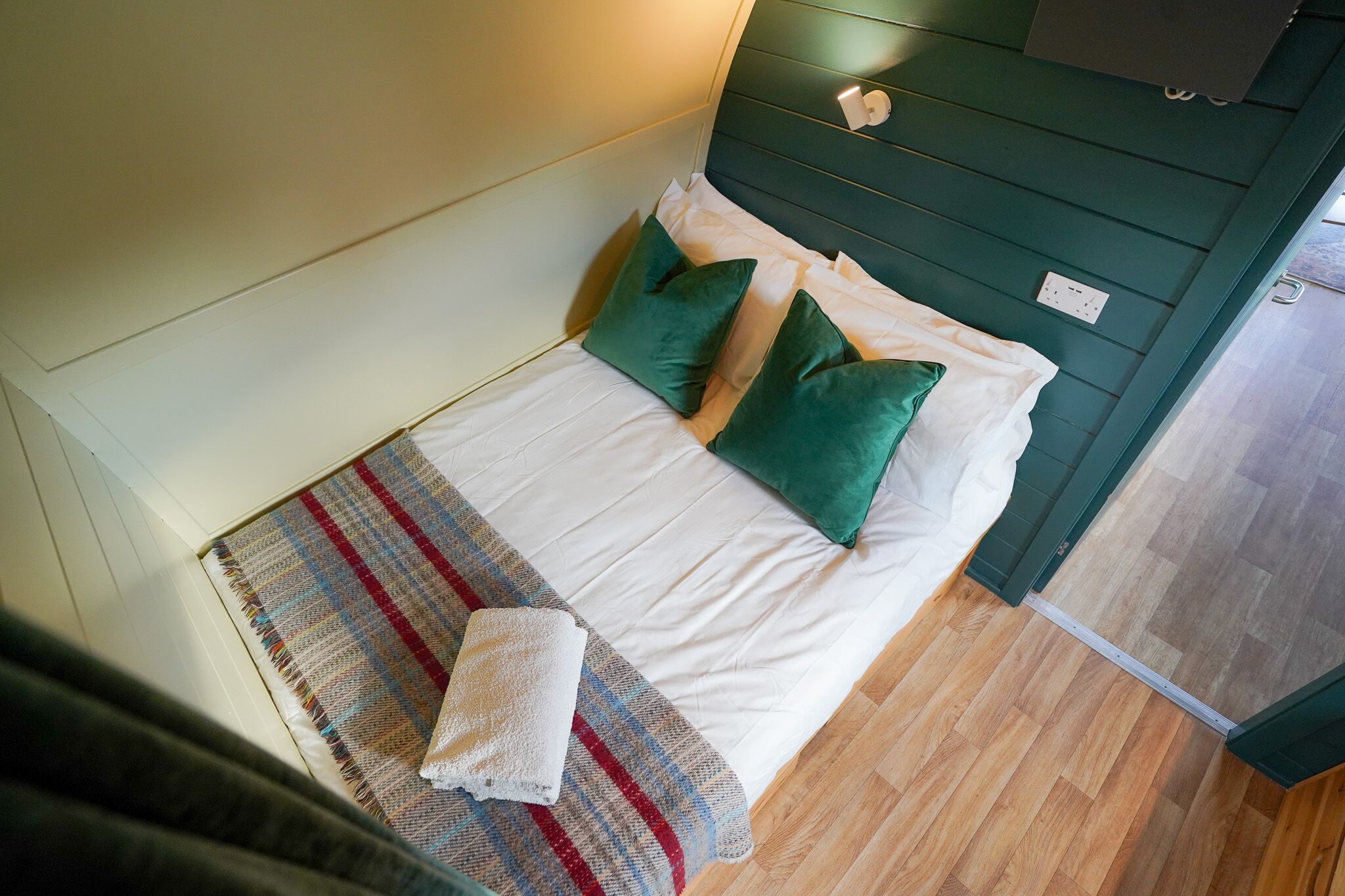 A bed with white linens and green pillows, a striped blanket, and a white towel on the floor.