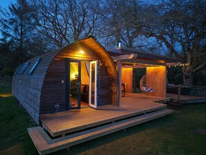 Une cabane en bois dotée d’un porche couvert, d’une chaise suspendue et d’un petit espace de détente extérieur.