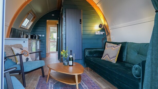 Un intérieur chaleureux avec un canapé, une table sur laquelle se trouvent une bouteille et des verres, et un coin cuisine sous un plafond en arc de cercle.