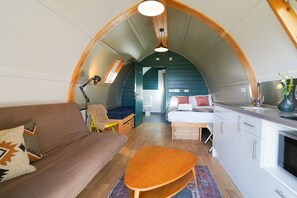 Et kompakt indretning med buet loft, sofa, lille træbord, seng og tekøkken.