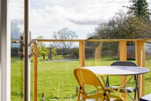 Una habitación con puerta de vidrio que da a un balcón con vista a un patio cubierto de césped y árboles.