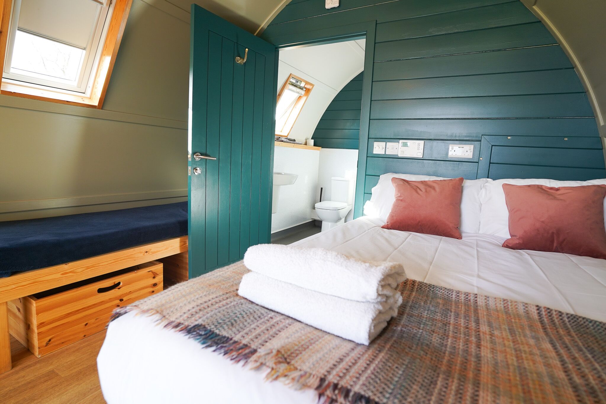 A bedroom with a bed, a bench, a window, and a door leading to a bathroom.