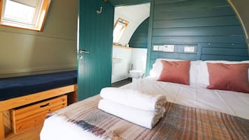 A bedroom with a bed, a bench, a window, and a door leading to a bathroom.