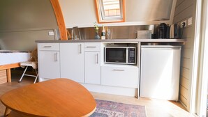 Een compacte keuken met witte kastjes, een magnetron, een koffiezetapparaat en een klein raam boven de gootsteen.