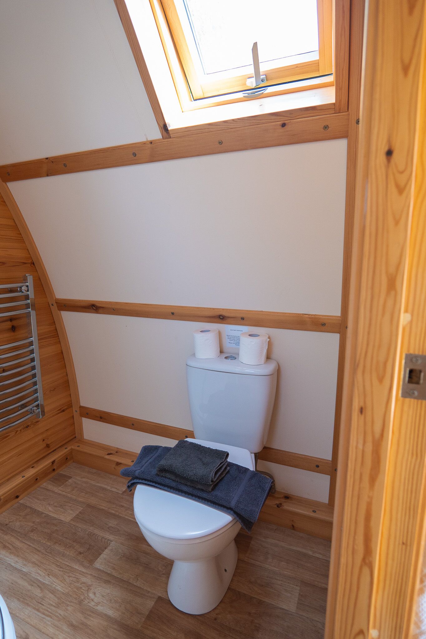 A compact bathroom with a skylight, wooden beams, and a white toilet.