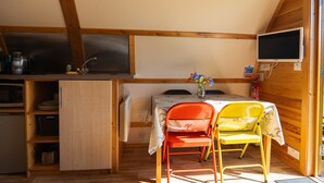 Cocina compacta con lavamanos, microondas y refrigerador pequeño. Hay una mesa con mantel floral y dos sillas. Un extintor está montado en la pared.