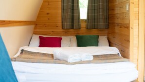 Una habitación acogedora con techo inclinado de madera, una cama con sábanas blancas y cortinas escocesas.