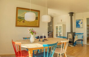 Un coin repas avec une table ronde en bois, des chaises colorées, un vase rempli de fleurs, des lampes suspendues et un tableau accroché au mur.