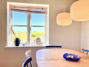 Et spiseområde med et stort vindue, et træbord, stole, en vase med planter og hængende lamper.