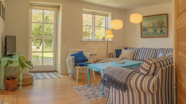 Una sala de estar acogedora con un sofá, una mesa y un televisor. Hay ventanas y un cuadro en la pared.