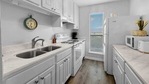 Una cucina moderna con mobili bianchi, un lavello in acciaio inossidabile, forno integrato e microonde.