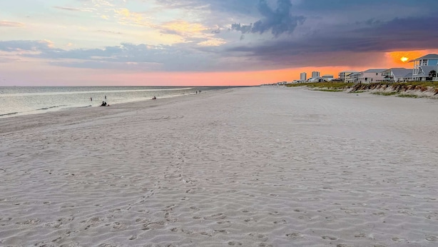 Una spiaggia con impronte, un tramonto e case sullo sfondo.