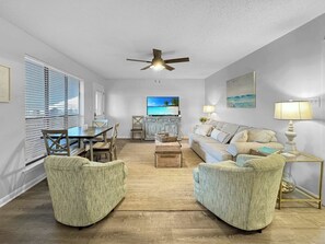 A spacious living room with a ceiling fan, a television, a sofa, and a dining area with a table and chairs.