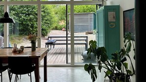A room with a large window, a table with chairs, a bench, and a teal cabinet. - Modern and cozy summer house in beautiful Balka (Nexø)