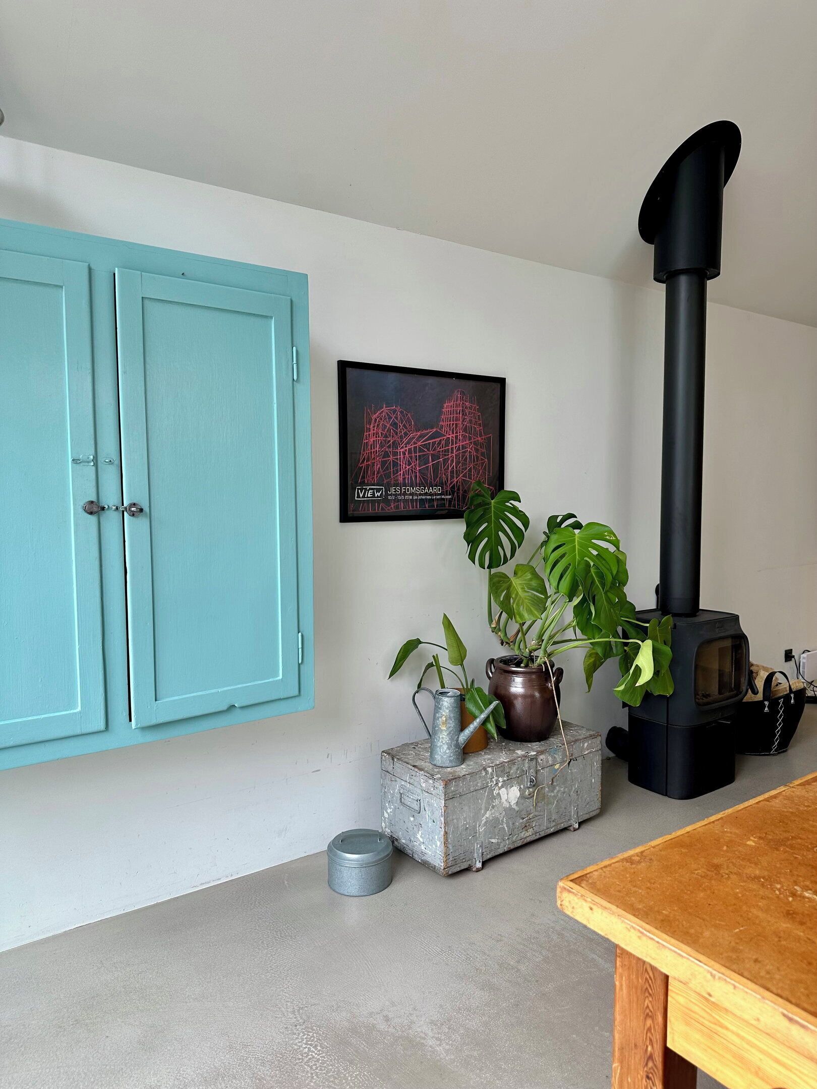 A room with a teal cabinet, a framed artwork, a black stove, and potted plants.