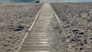 A wooden boardwalk leading to a beach with footprints and a distant view of the ocean. - Modern and cozy summer house in beautiful Balka (Nexø)