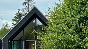 A modern house with a large glass window, a wooden deck, and a bench. - Modern and cozy summer house in beautiful Balka (Nexø)