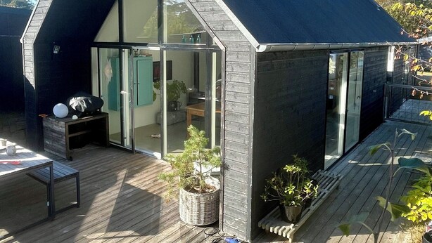 A modern house with a steeply pitched roof, large glass windows, and a wooden deck. - Modern and cozy summer house in beautiful Balka (Nexø)