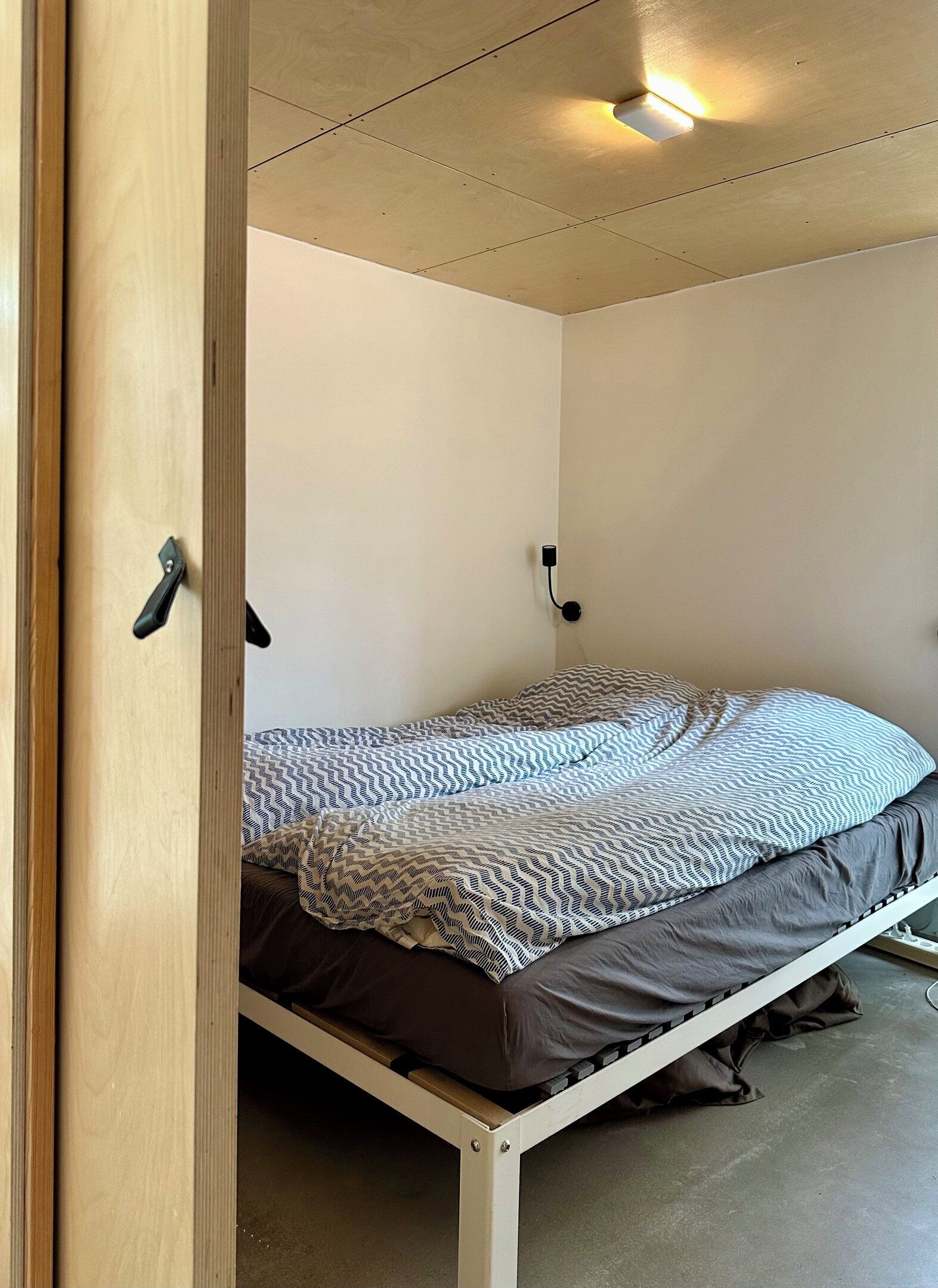 Un letto singolo con copriletto decorato, una lampada a parete e l'architrave di una porta.